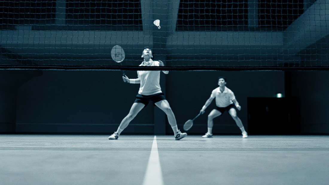 Badminton player mid jump smash in a packed arena