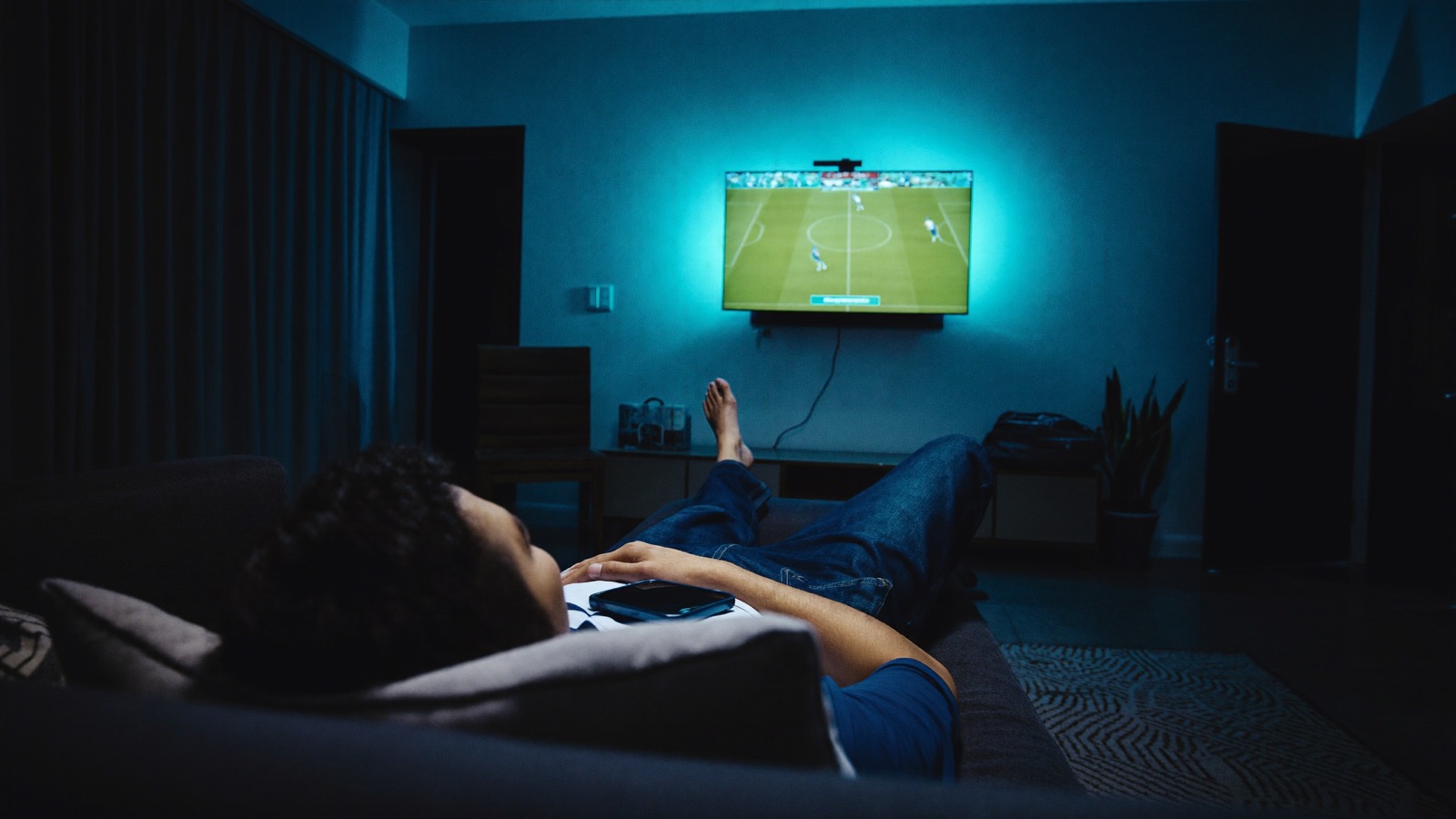 Family and friends watching sport on television at home with phones in hand